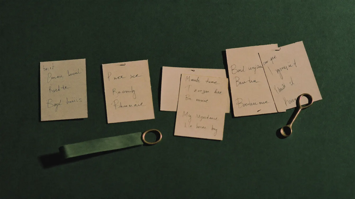 Four handwritten index cards laid out on a green desk surface with a brass pin.